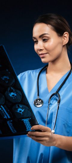 Young concentrated lady doctor with stethoscope looking at x-ray image isolated